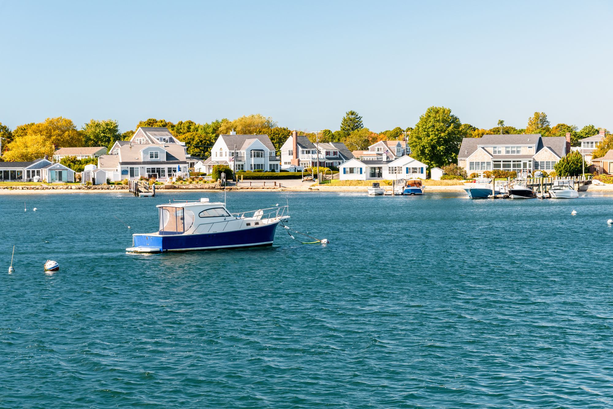 Shingled homes along a Cape Cod harbor with a boat on a mooring